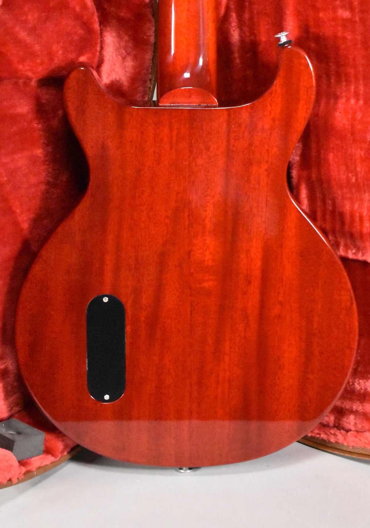 The back of a glossy, deep cherry red double-cut guitar with visible wood grain, a black control plate, and a strap button.