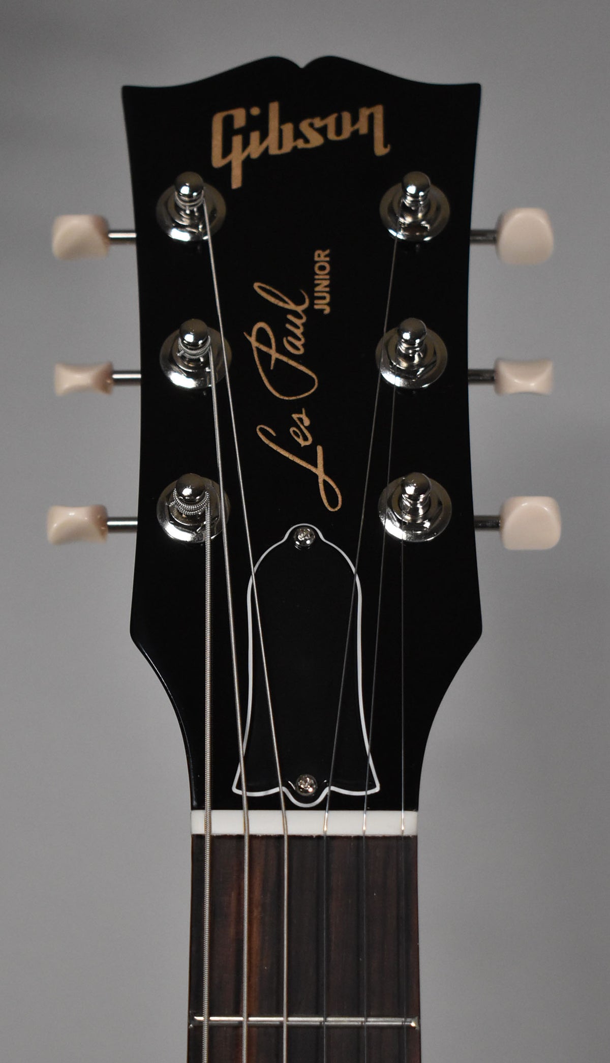 Close-up of the black headstock with cream tuners, chrome hardware, and a white truss rod cover, showing the top of the fretboard.