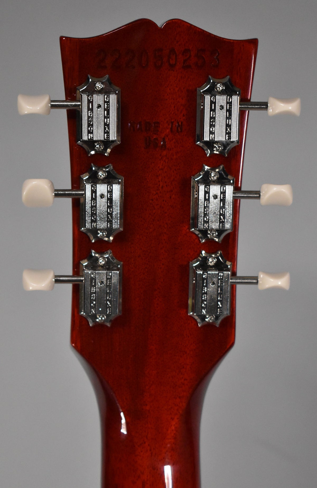 The back of a cherry red headstock with six cream-buttoned tuners, showing light finish checking and a serial number.