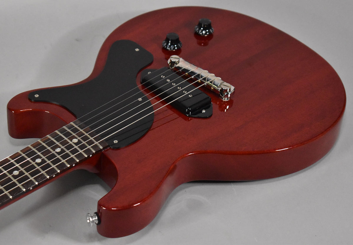 The cherry red double-cutaway electric guitar is angled from the lower bout, showing its black pickguard, P90 pickup, and two control knobs.