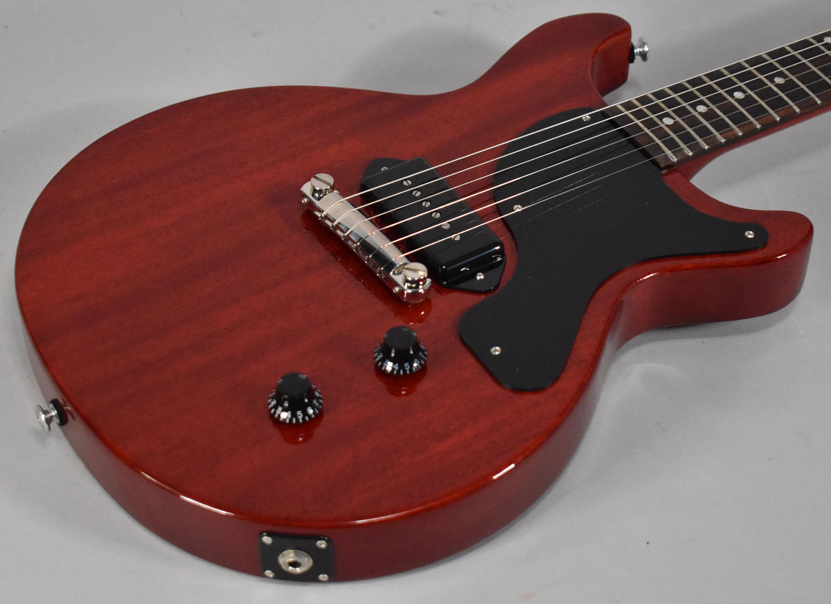 The cherry red guitar body, with a black pickguard and P90 pickup, is angled from the lower bout towards the neck.