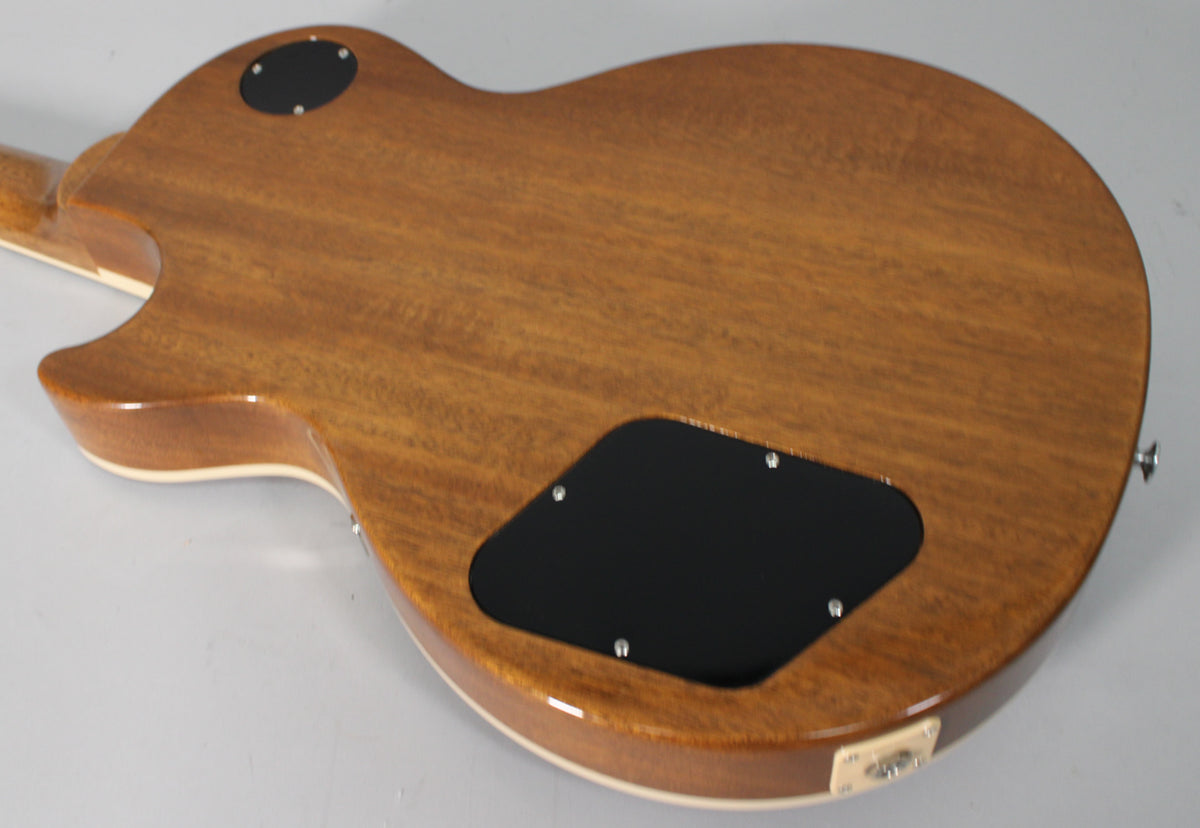 The back of a Les Paul guitar, showing a glossy, reddish-brown wood grain finish with cream binding and two black control cavity covers.