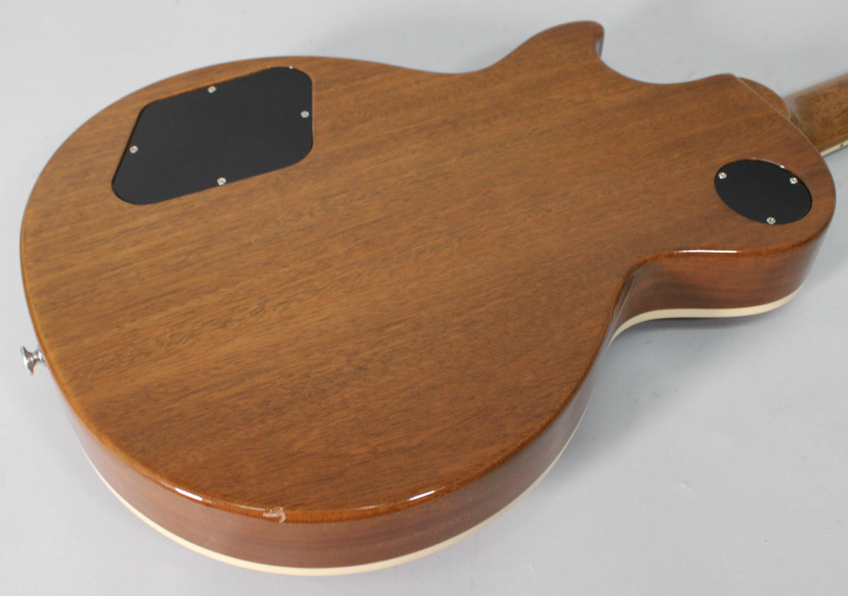 The guitar's back, a matte brown with a glossy edge, shows two black control plates and a small chip on the lower bout.