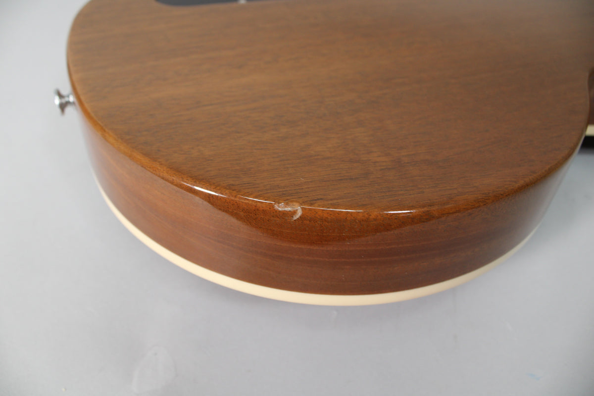 Close-up of the guitar's lower bout, showing a small chip in the glossy burgundy finish near the cream binding.