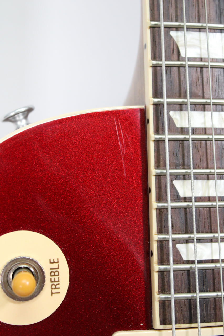 Close-up of the upper body in sparkling burgundy with visible scratches, showing the cream pickup selector switch set to "TREBLE" and part of the fretboard.