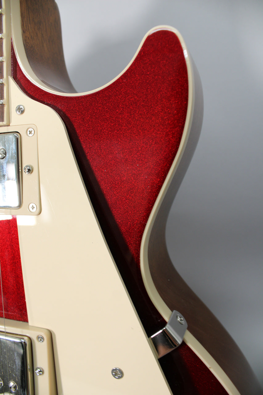 Close-up of the guitar's lower bout, showing the sparkling burgundy finish, cream binding, and part of the pickguard and bridge pickup.