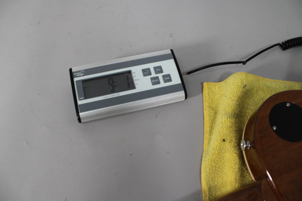 A digital scale displays "9.1" next to the guitar's lower bout, resting on a yellow cloth, showing the back of the control cavity cover.