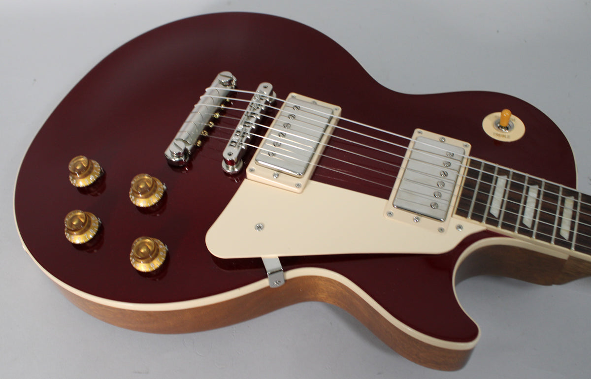 The upper body of a glossy sparkling burgundy guitar, showing cream binding, pickguard, and pickup rings, with gold top hat knobs.