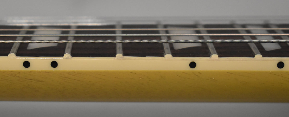 Close-up of the guitar neck's side, showing the dark fretboard with trapezoid inlays, cream binding, and black side dots.