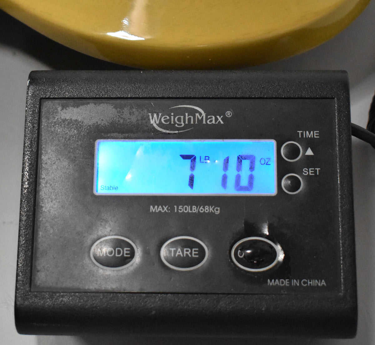 Close-up of a digital scale displaying "7 LB. 10 OZ." with a portion of the guitar's yellow body visible above.