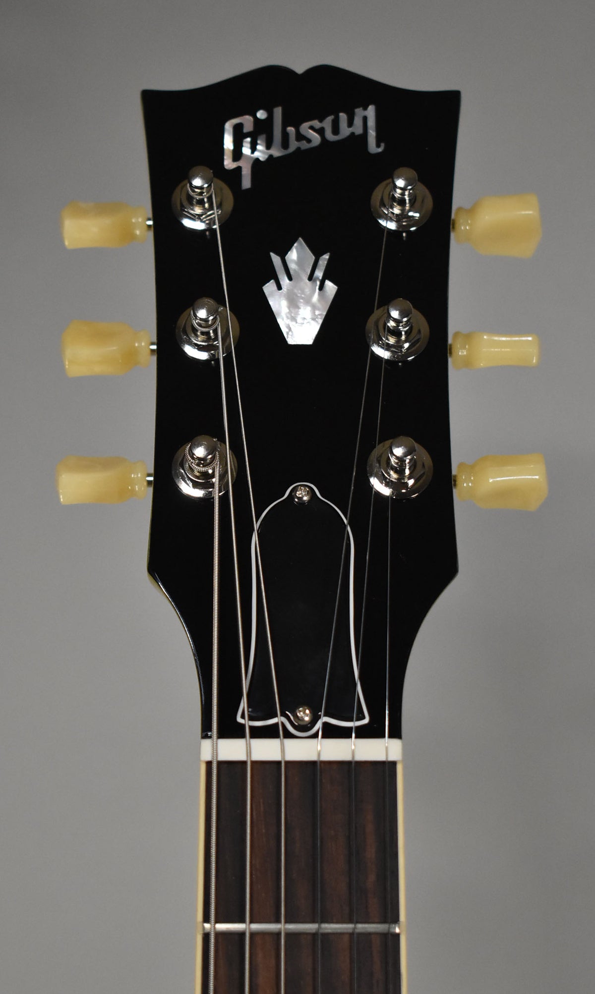The black headstock, with mother-of-pearl inlay and six cream tuning pegs, is viewed from the front.