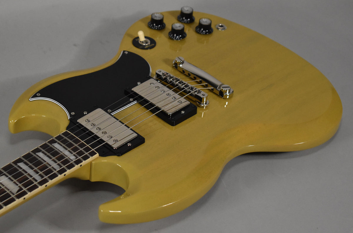 The TV Yellow SG body, with a black pickguard and chrome hardware, is angled from the lower left, showing the neck and controls.