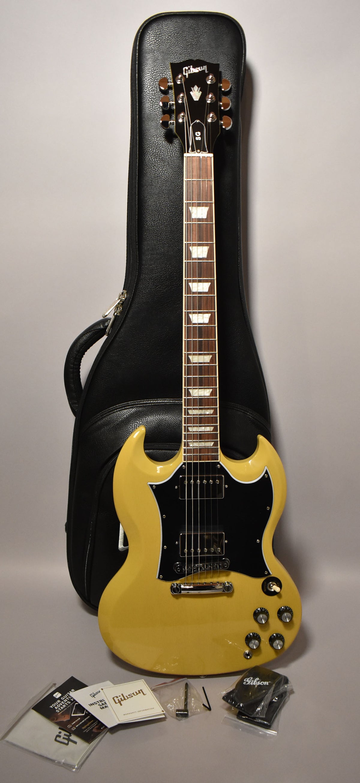 Full-length view of a glossy TV Yellow SG with a black pickguard, chrome hardware, and trapezoid inlays, leaning on a black gig bag.