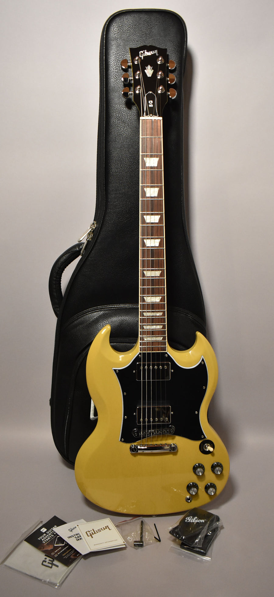 Full-length view of a glossy TV Yellow SG with a black pickguard, chrome hardware, and trapezoid inlays, leaning on a black gig bag.