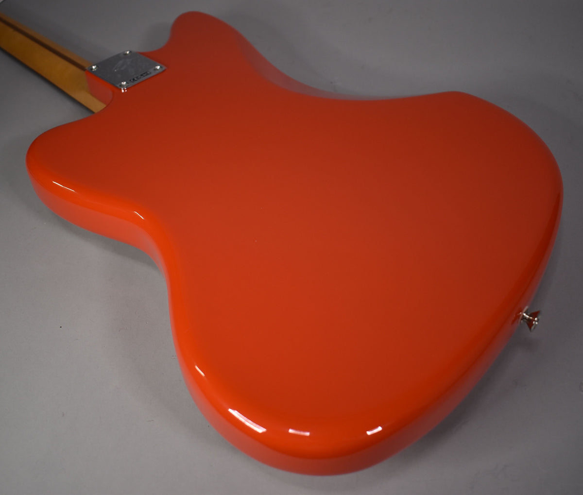 Rear view of a glossy coral red Jazzmaster body, showing the chrome neck plate and strap button, with a light wood neck.