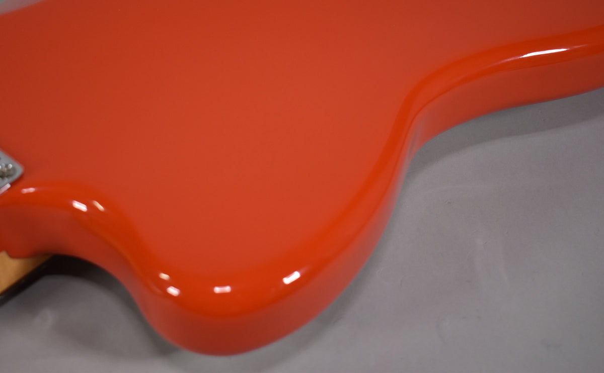 Close-up of the Jazzmaster's glossy coral red body, showing the upper horn and part of the neck joint from a high angle.