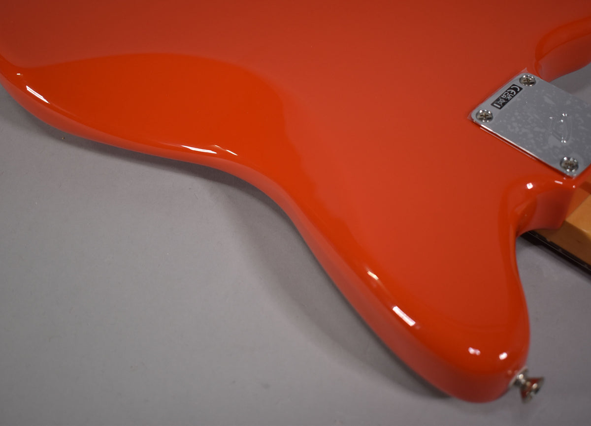 The lower bout of a glossy coral red Jazzmaster, showing the chrome neck plate and strap button.