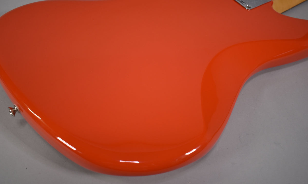 The upper back of a glossy coral red Jazzmaster body, with a chrome strap button on the lower bout and a neck plate visible at the top.
