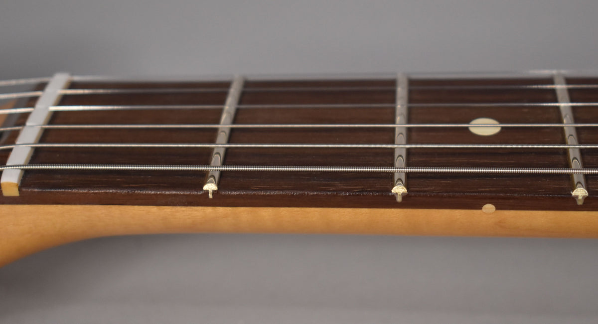 Close-up of the Jazzmaster's dark rosewood fretboard with white dot inlays, showing the nut, frets, and six strings.