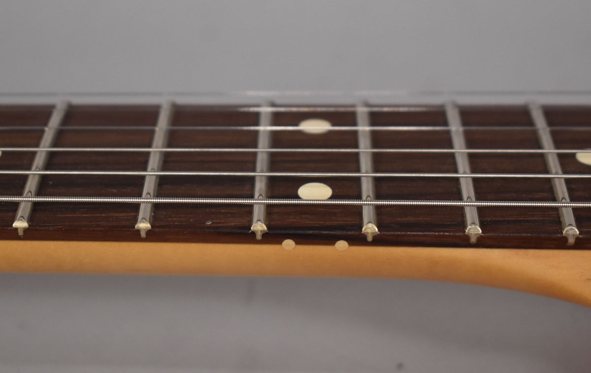 Close-up of the guitar's dark fretboard with light fret markers and strings, showing the light-colored neck binding and side dots.
