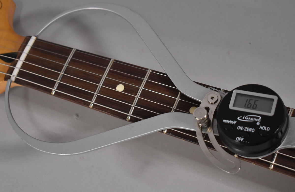 Close-up of the guitar's dark fretboard with white dot inlays, showing a digital fret rocker measuring fret height at 1.66mm.