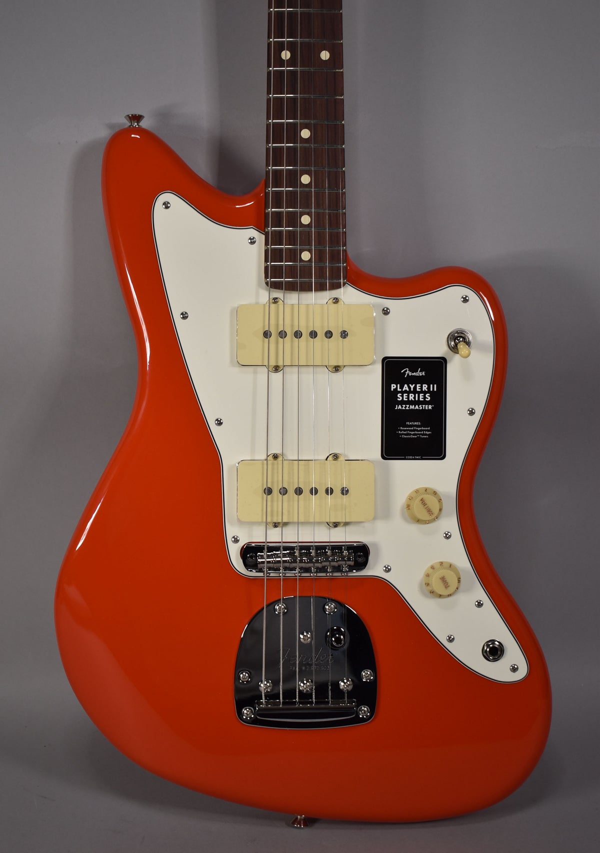 A coral red Jazzmaster with a white pickguard, two cream P90 pickups, and chrome hardware, viewed from the front.