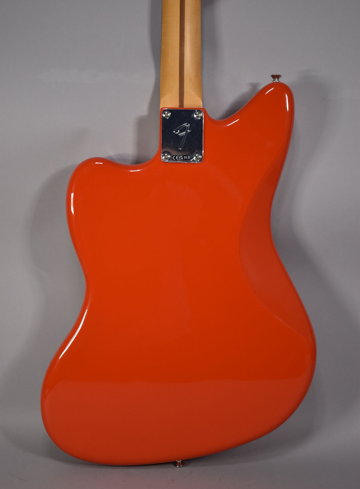 The back of a glossy coral red Jazzmaster body, with a chrome neck plate and a light wood neck.
