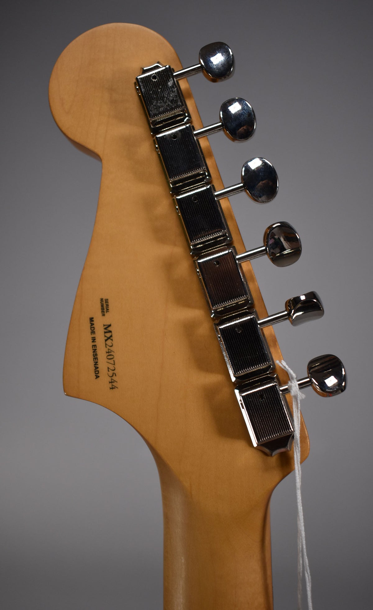 Close-up of the guitar's light wood headstock and neck, showing six chrome tuning machines and a white string tag.