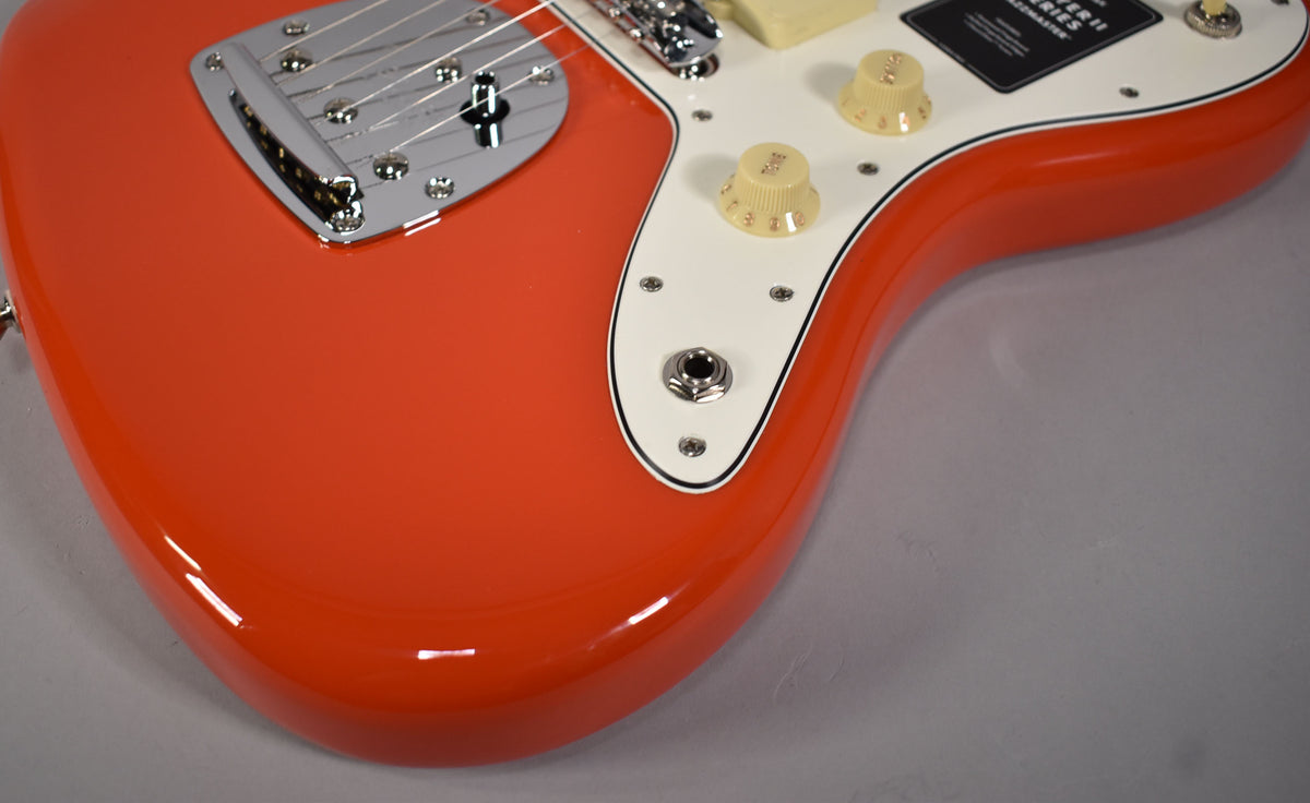 Upper right body of a glossy coral red Jazzmaster, showing the chrome bridge, cream pickguard, and two cream control knobs.