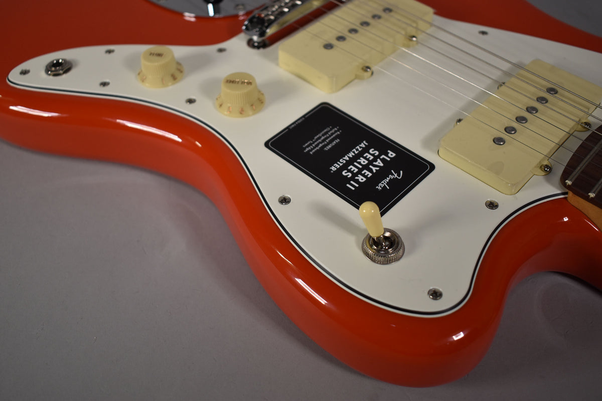 Close-up of the glossy coral red Jazzmaster body, showing the white pickguard, two cream P90 pickups, and three cream control knobs.