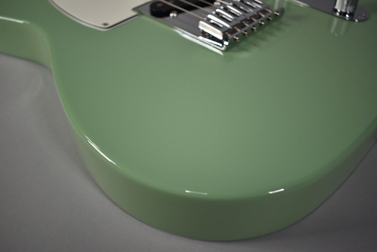 Upper body of a glossy birch green Telecaster, showing the chrome bridge and a sliver of the white pickguard.