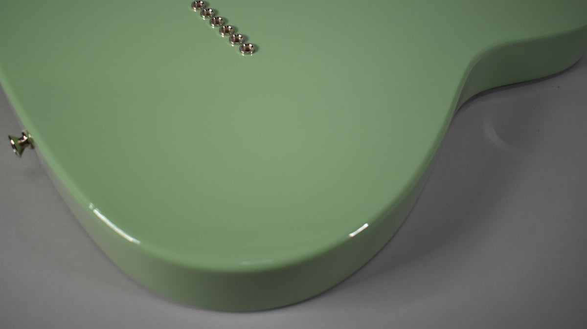The glossy birch green Telecaster body is angled from the lower left, showing the output jack and six string ferrules.