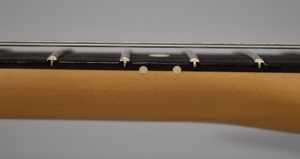 Close-up of the guitar's maple neck and dark fretboard, showing two white side dots and several frets with strings.