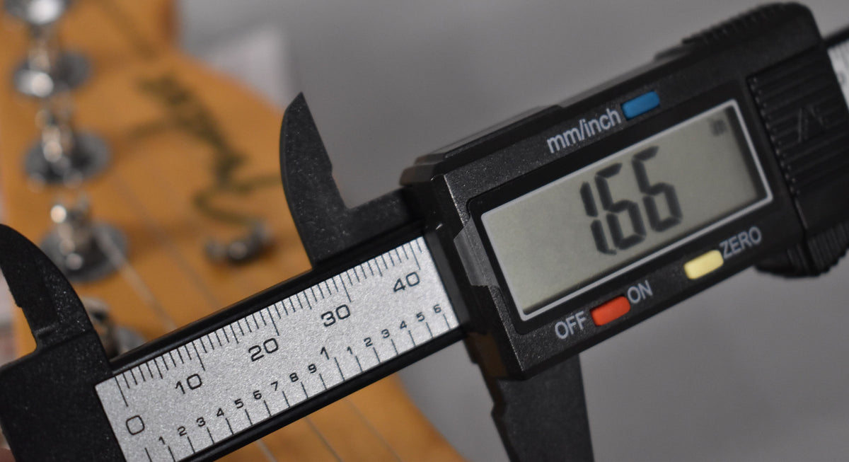 A digital caliper measures the nut width of the birch green Telecaster's headstock, displaying "1.66" on its screen.