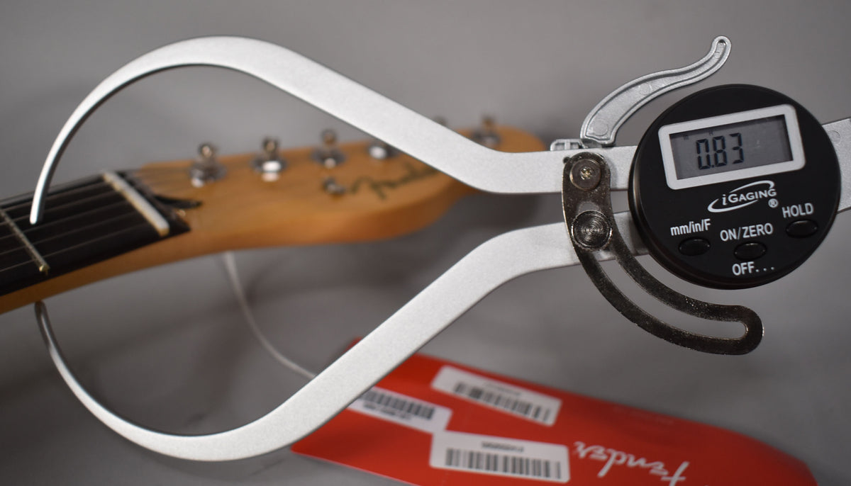 A digital caliper measures the string height at the nut of a Telecaster, showing 0.83mm, with a red hang tag visible below.