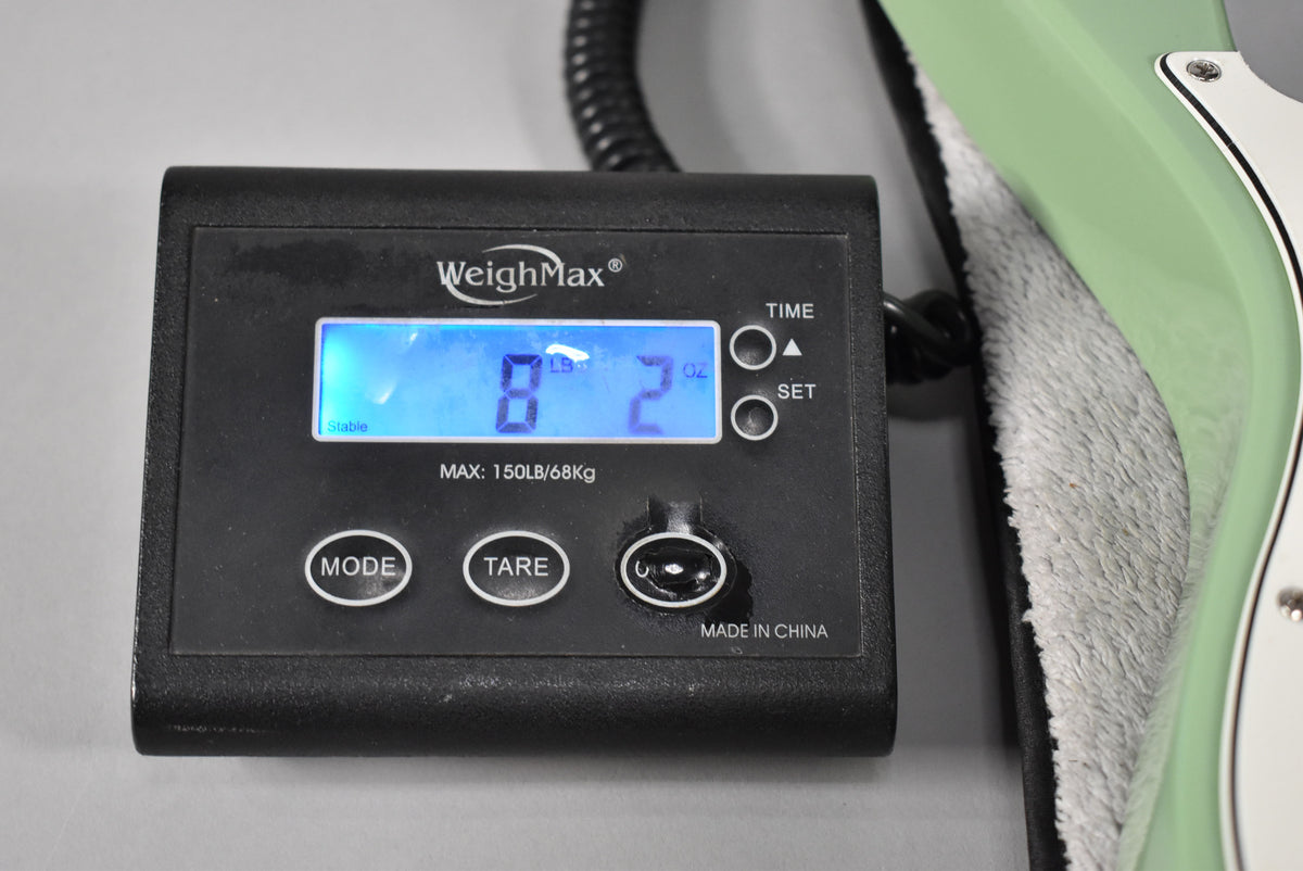 A close-up of a digital scale displaying "8 LB 2 OZ" with the Birch Green Telecaster's body resting on a soft grey cloth.