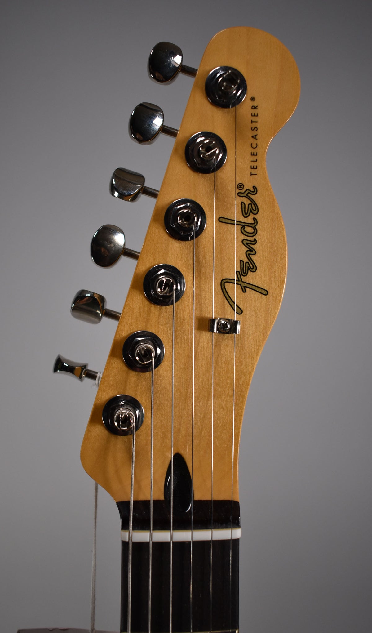 Close-up of a Telecaster headstock with "Fender" and "TELECASTER" visible, showing tuning pegs, strings, and the top of the fretboard.