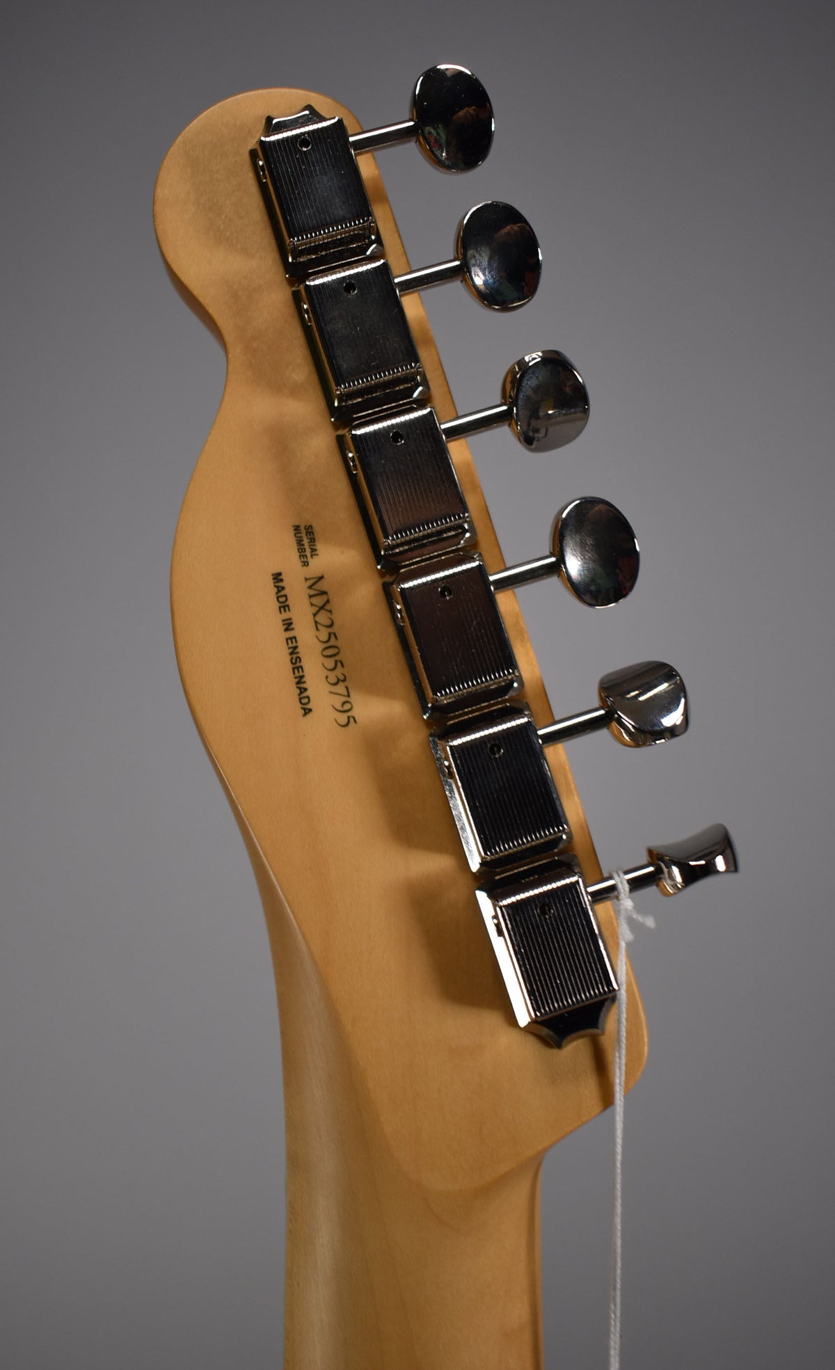 The back of the guitar's headstock and neck, showing six chrome tuners and a serial number stamped on the wood.