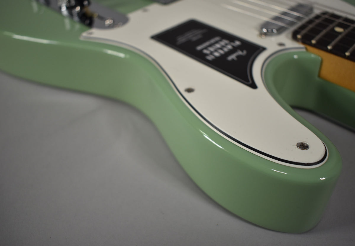 Close-up of the lower bout of a glossy birch green Telecaster, showing the white pickguard with black trim.