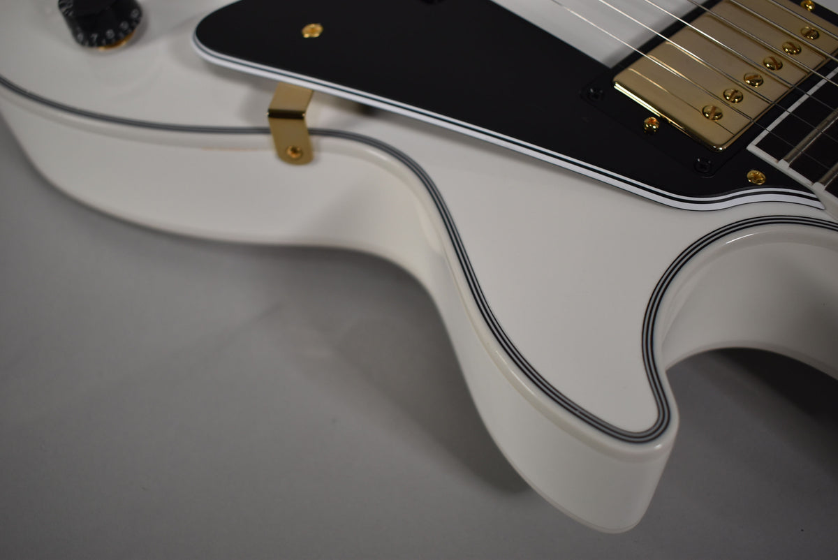 Close-up of the Alpine White body with black binding, gold hardware, black pickguard, and a single black control knob.