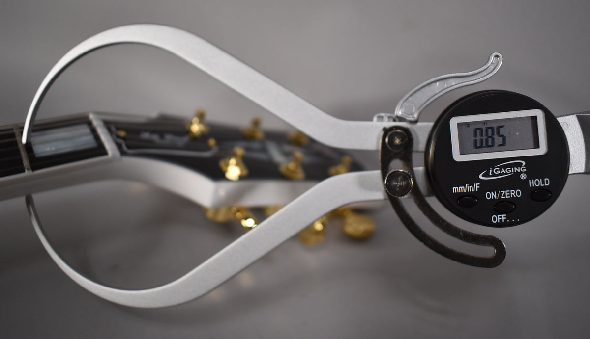 Close-up of a digital caliper measuring the string height at the first fret of the Alpine White Les Paul's neck, showing 0.85mm.
