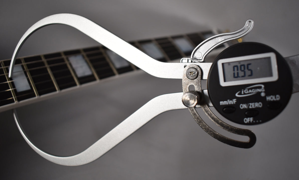 A digital caliper measures the string height at the fretboard, displaying "0.95" on its screen.