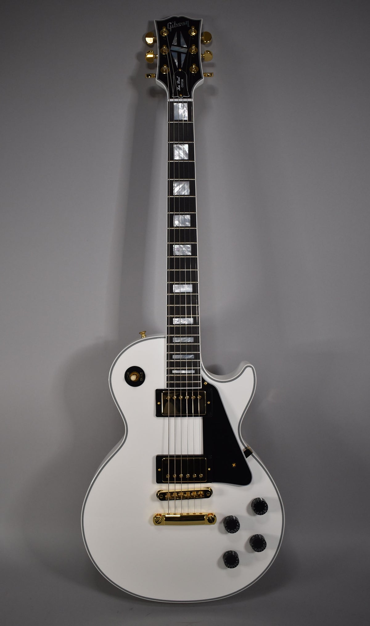 Full-length view of a glossy white Les Paul with gold hardware, black pickguard, and trapezoid fretboard inlays.