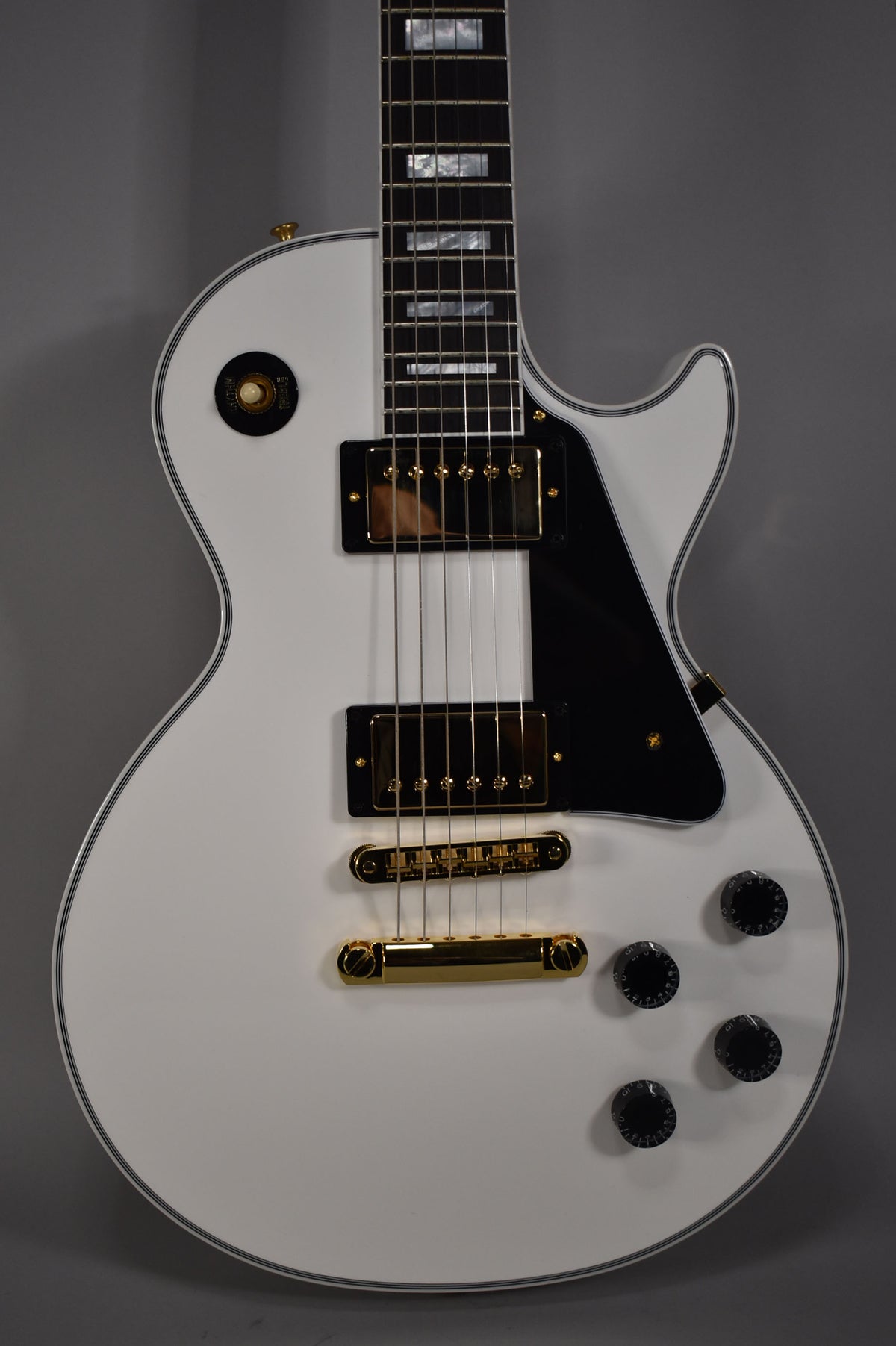 Close-up of the Alpine White Les Paul's body, showing gold hardware, black pickguard, and four black control knobs.