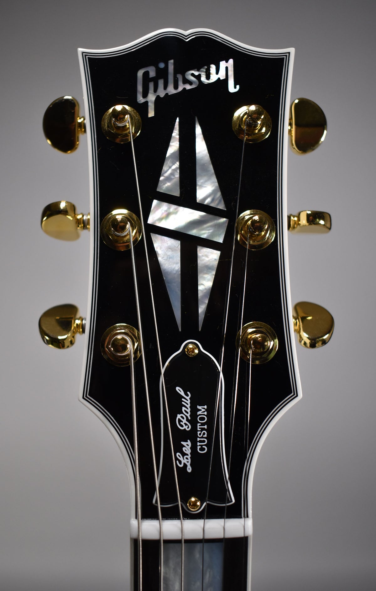Close-up of the black headstock with white binding, gold tuners, mother-of-pearl inlays, and a bell-shaped truss rod cover.
