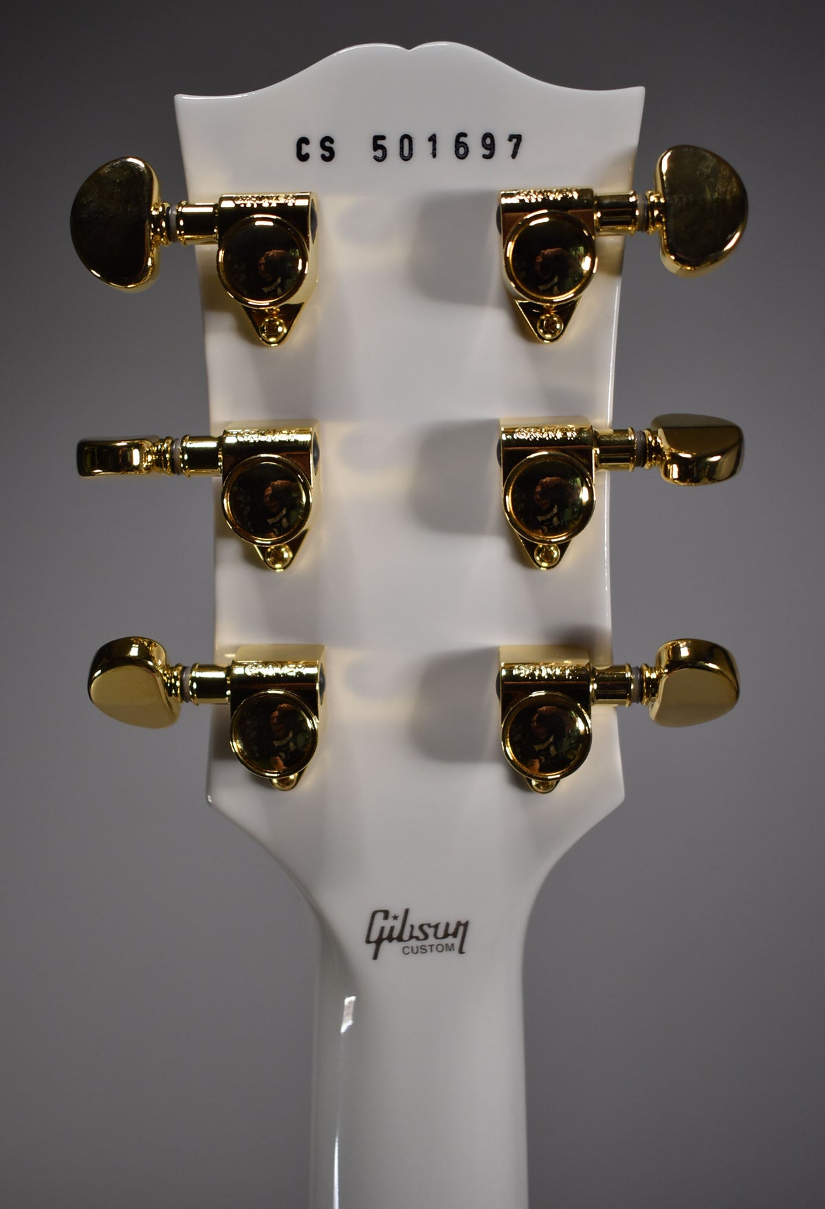 Rear view of the Alpine White headstock and top of the neck, showing six gold tuners and a black serial number.