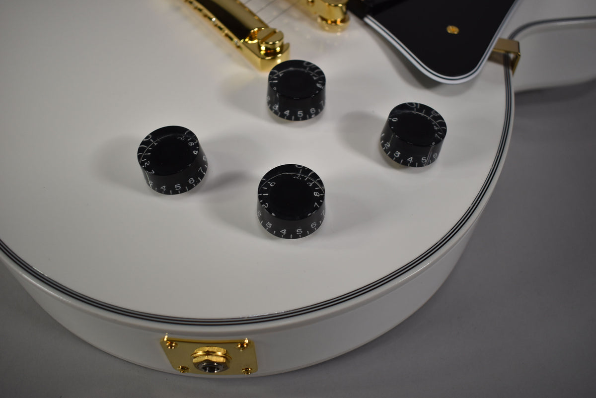 Close-up of the Alpine White body with four black numbered control knobs, a gold output jack, and black pinstriping along the edge.