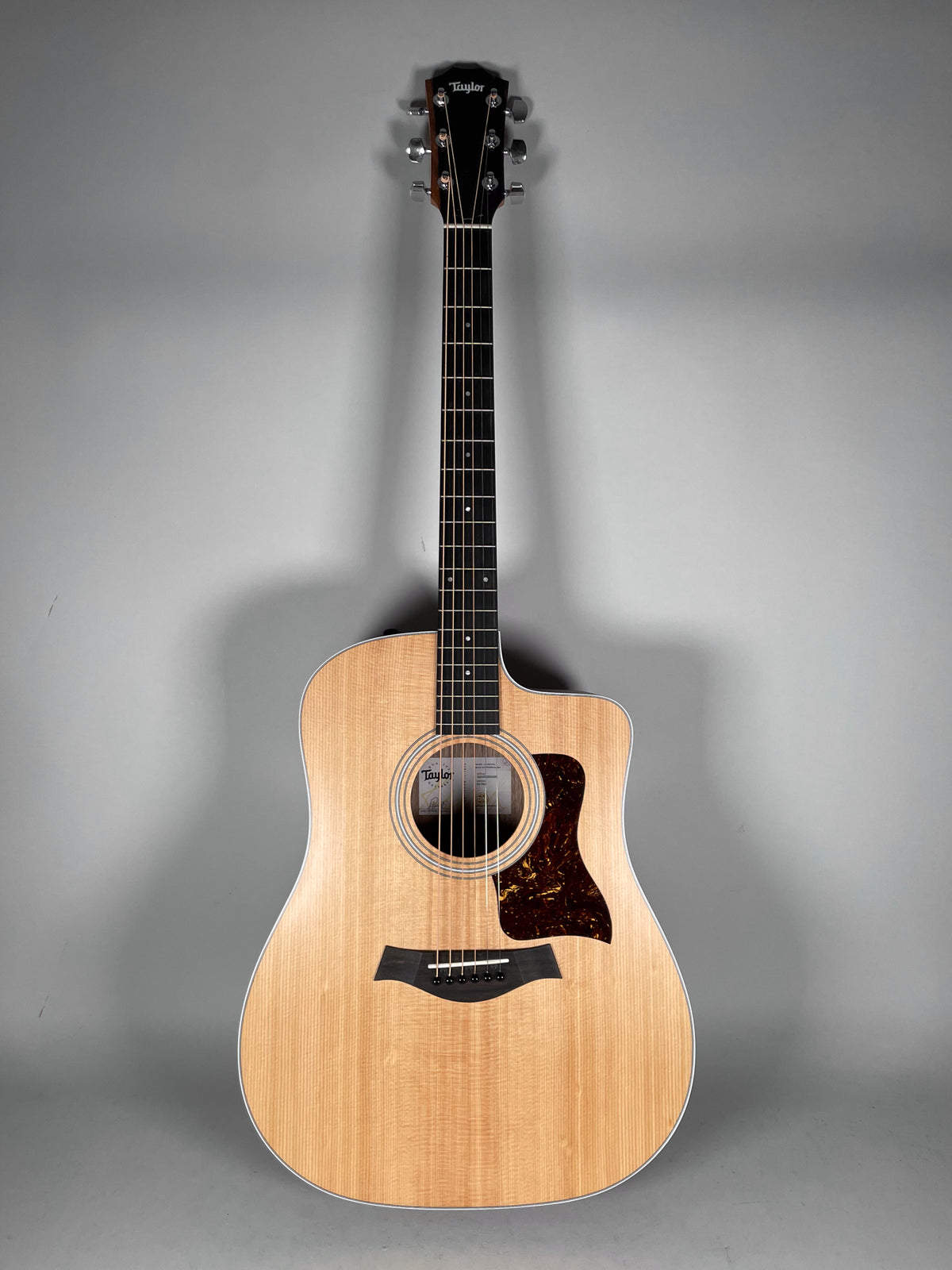 A full-frame shot of a natural finish Taylor acoustic guitar with a cutaway, against a plain gray background.