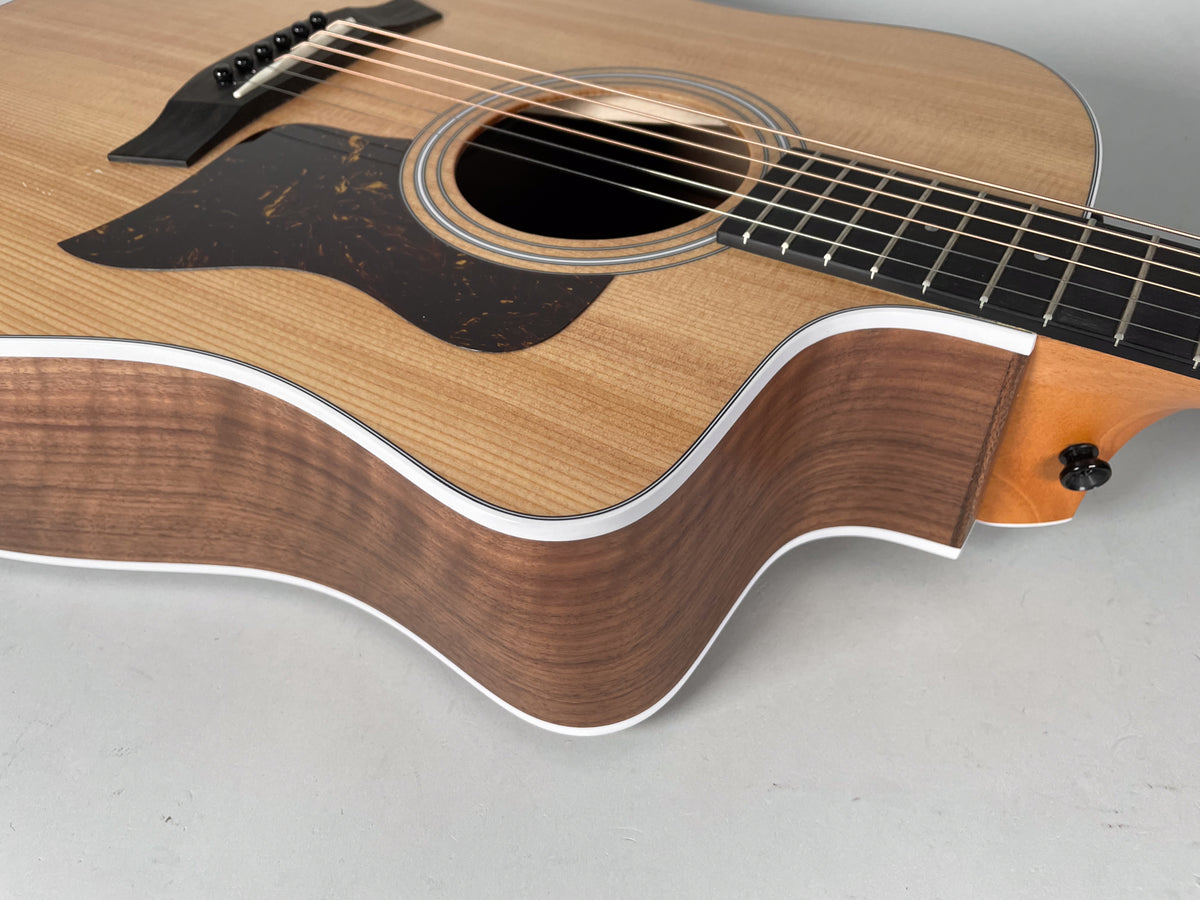 Close-up of the natural finish acoustic guitar's lower bout and cutaway, showing the dark wood grain and white binding.
