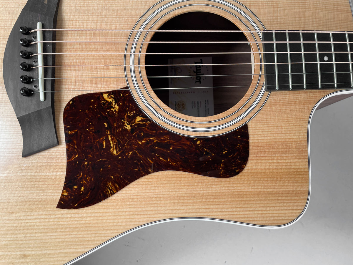 Close-up of the natural finish acoustic guitar's body, showing the soundhole, tortoiseshell pickguard, and black bridge with white pins.